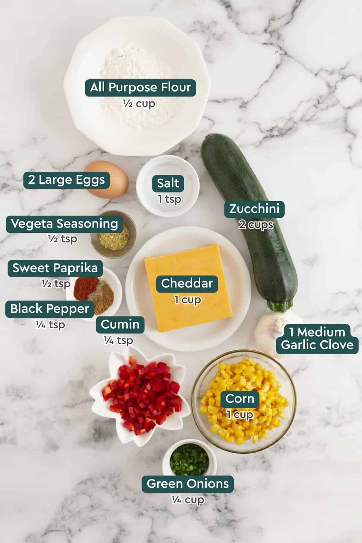 Ingredients for zucchini corn fritters, including flour, zucchini, salt, eggs, vegeta, seasonings, cheddar, garlic, corn, green onions.