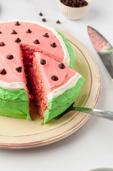 A slice of watermelon cake being lifted from a platter.