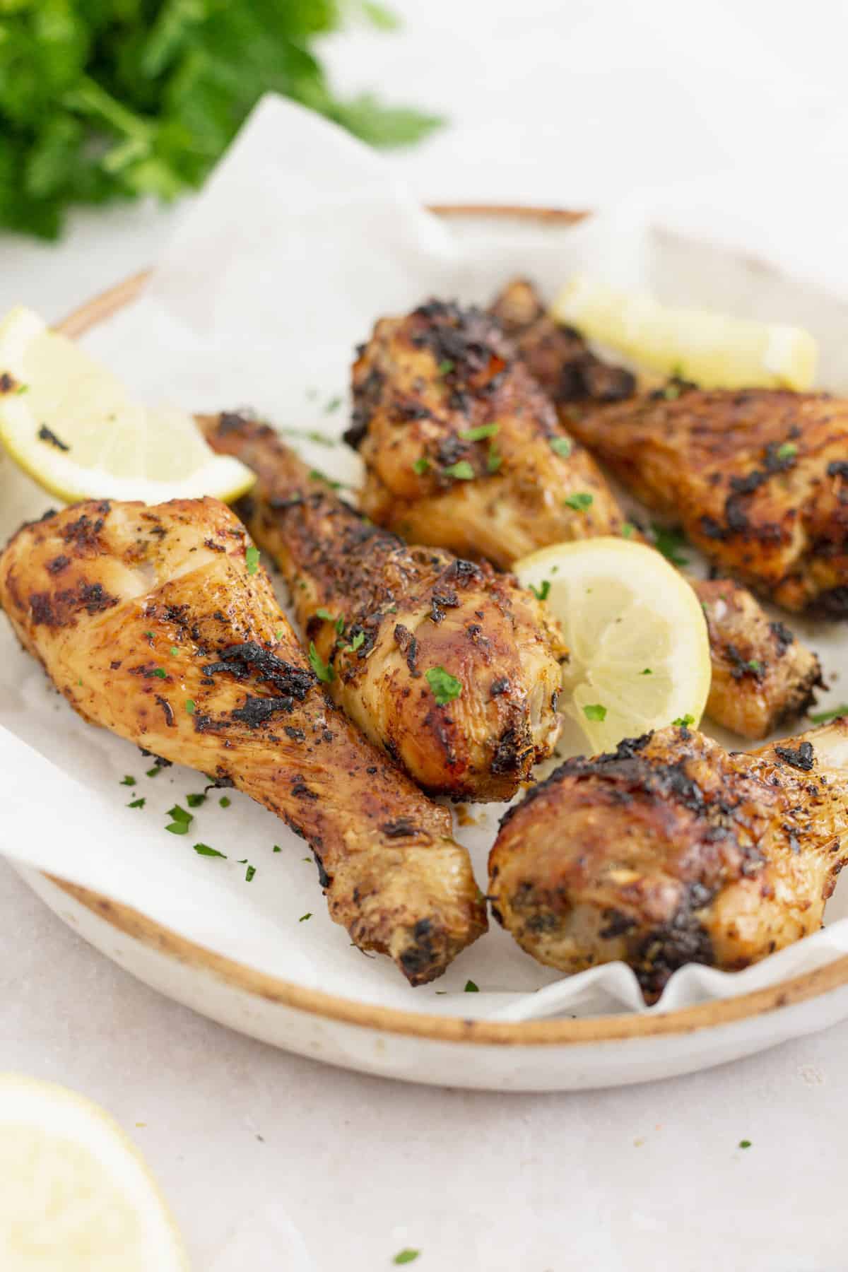 close up image of air fryer chicken drumsticks served on a plate topped with lemon slices and parsley