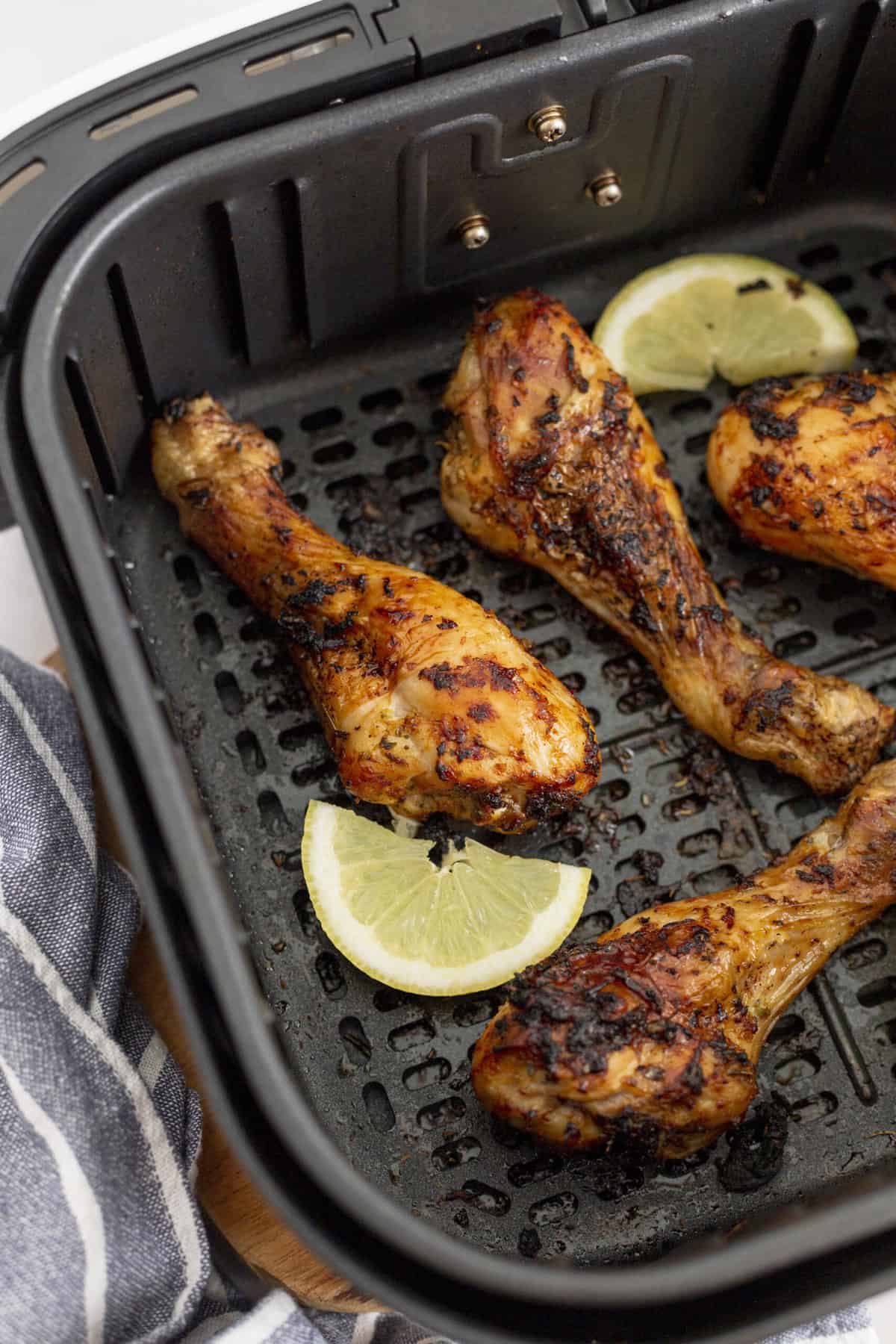 close up image of air fryer chicken drumsticks in a an air fryer basket with lemon slices