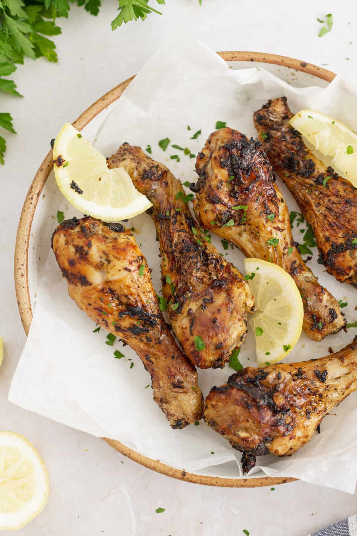 top down image of air fryer chicken drumsticks served on parchment paper on a plate with lemon wedges and parsley