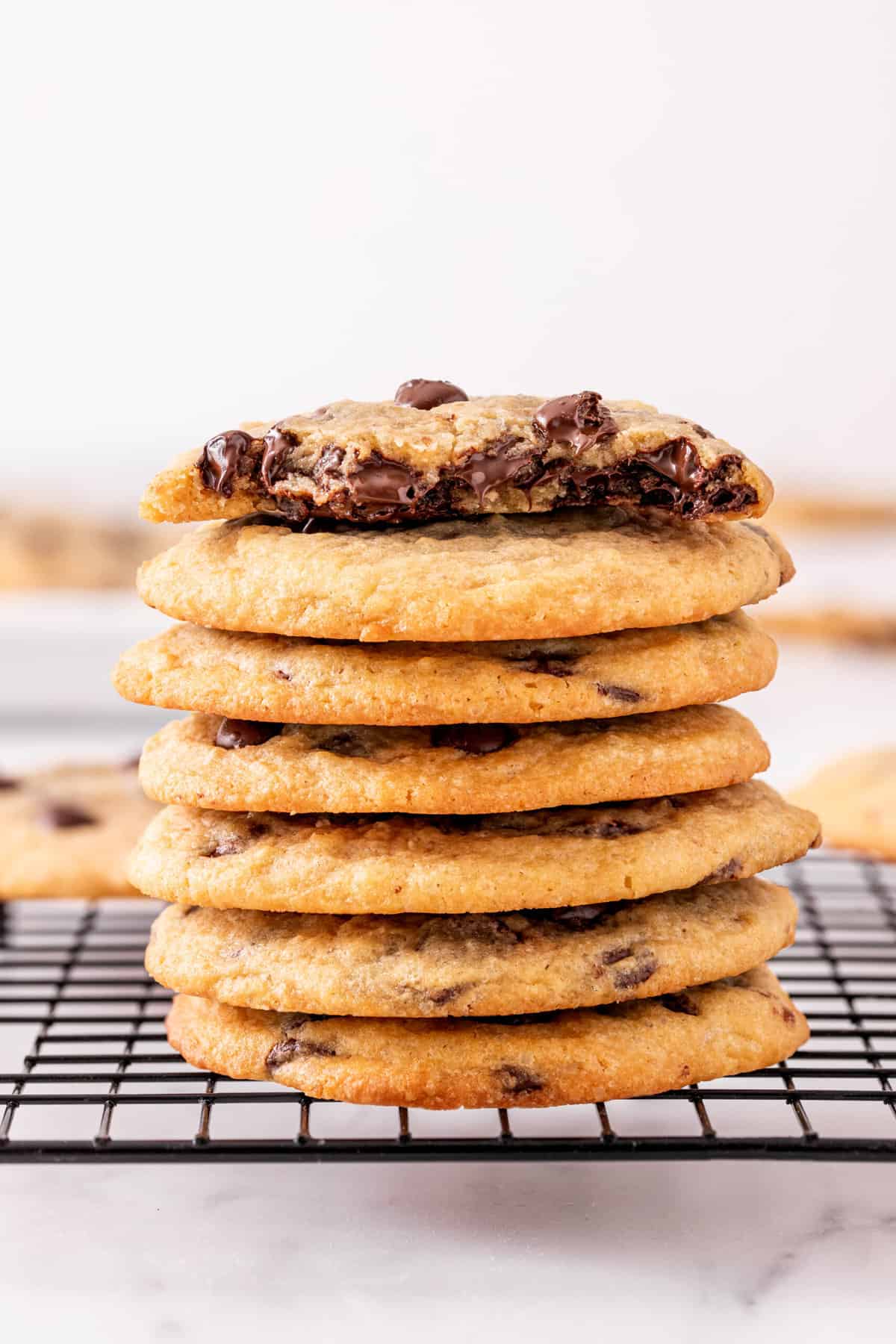 Close up of a stack of seven crispy and chewy chocolate chip cookies on a wire cooling rack.