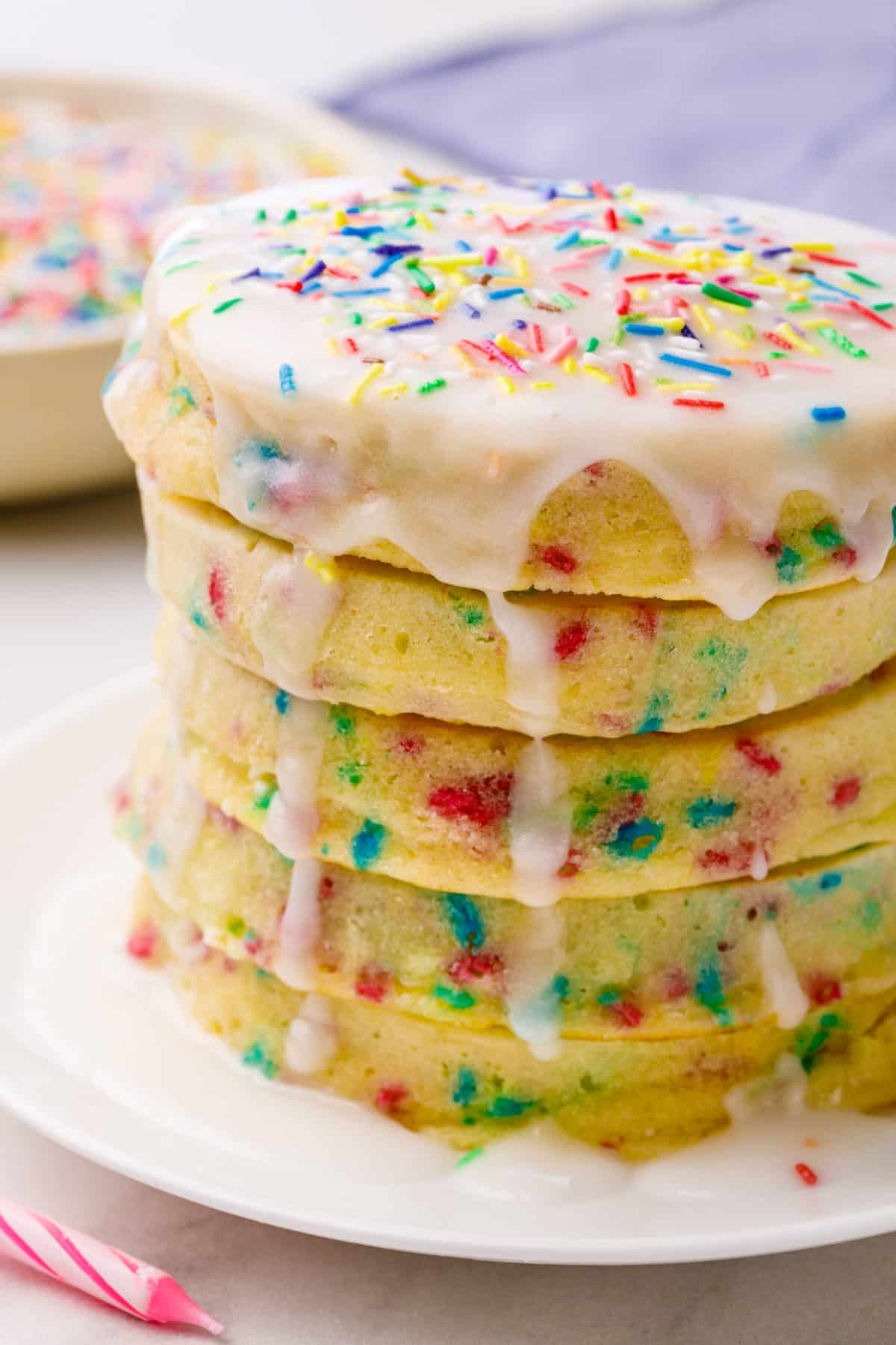 close up image of a stack of birthday cake pancakes served on a white round plate