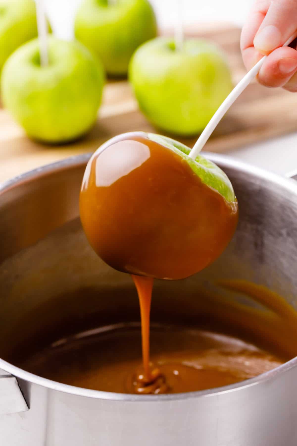 granny smith apple on a stick dipping into caramel sauce