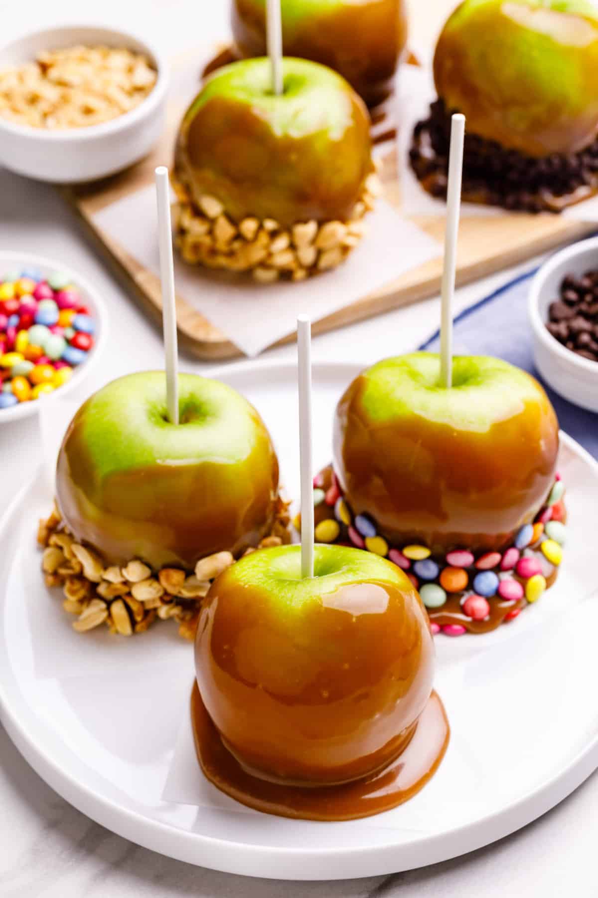 three decorated caramel apples sitting on a white round plate