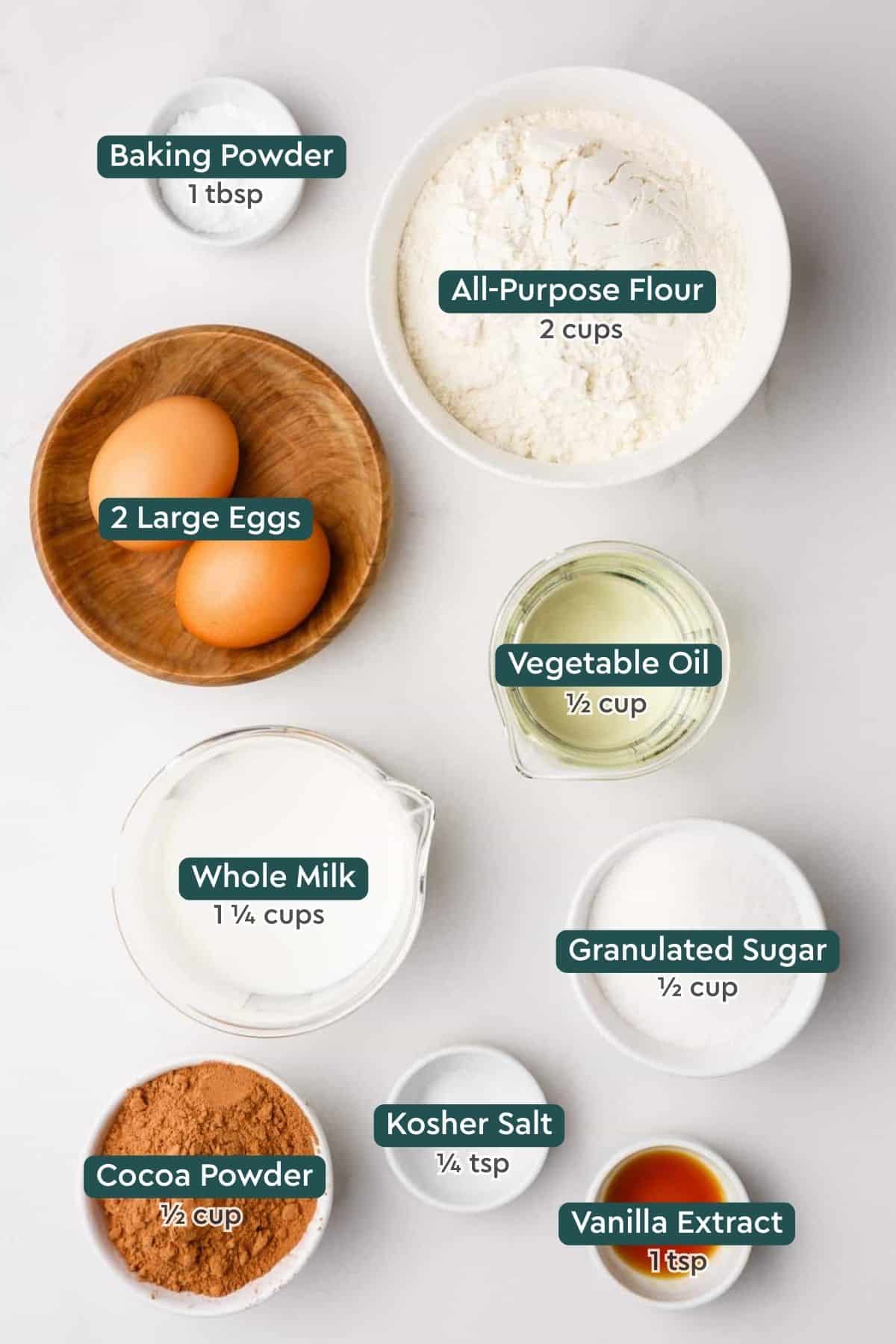 All of the ingredients for homemade chocolate waffles in bowls on a white countertop.