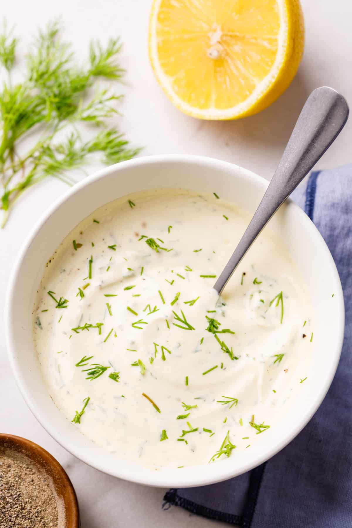 close up top down view of lemon dill sauce served in a white bowl with a silver spoon
