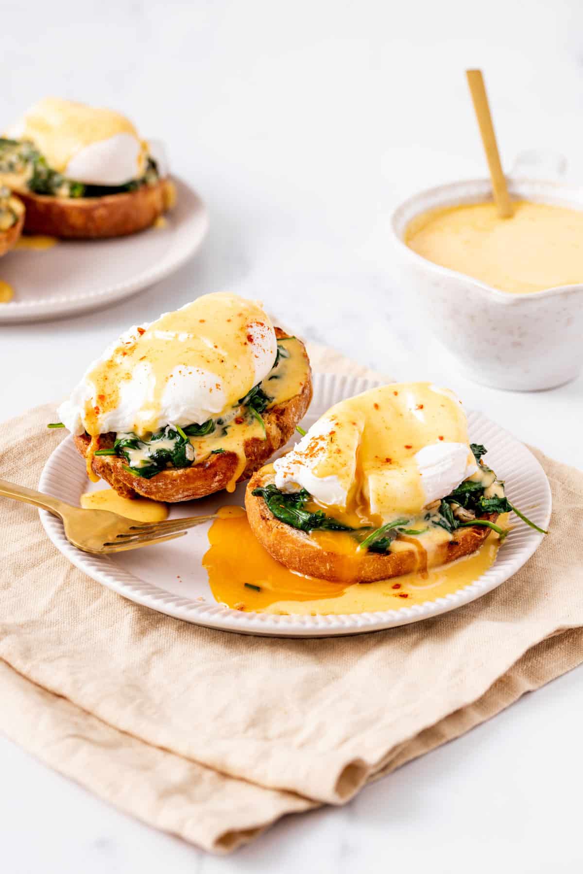 two eggs florentine served on a white plate with a gold fork, sitting on a beige kitchen towel