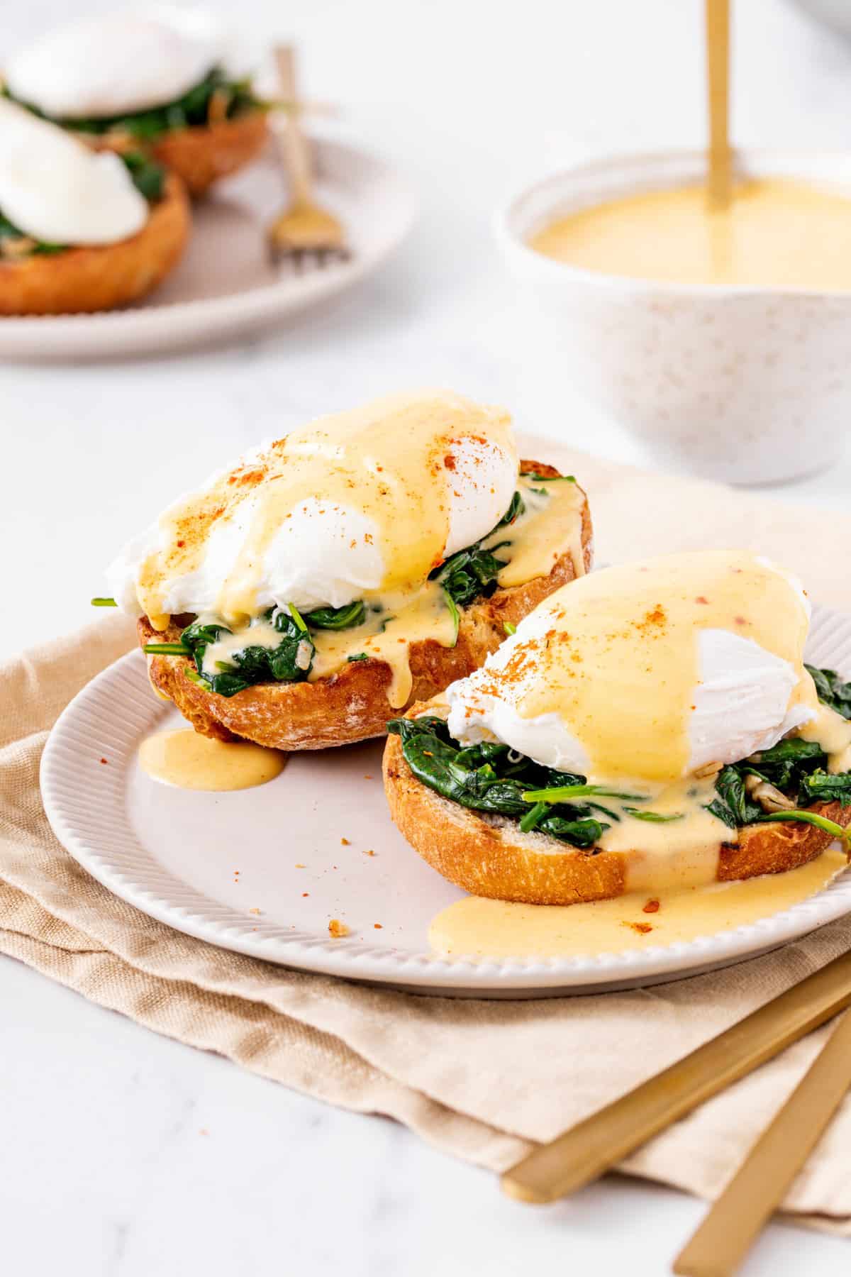 two eggs florentine served on a white plate sitting on a beige kitchen towel
