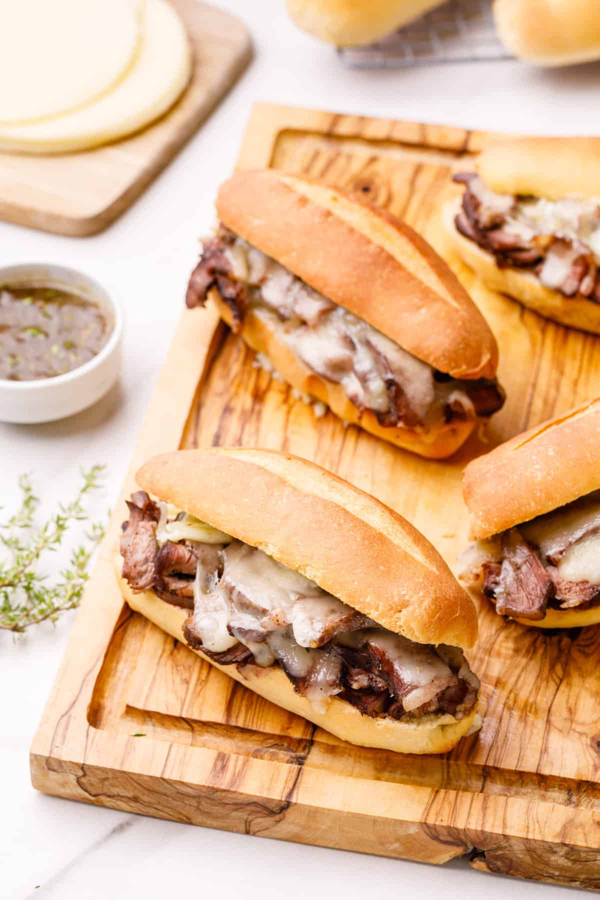 several prepared french dip sandwiches sitting on a wooden cutting board