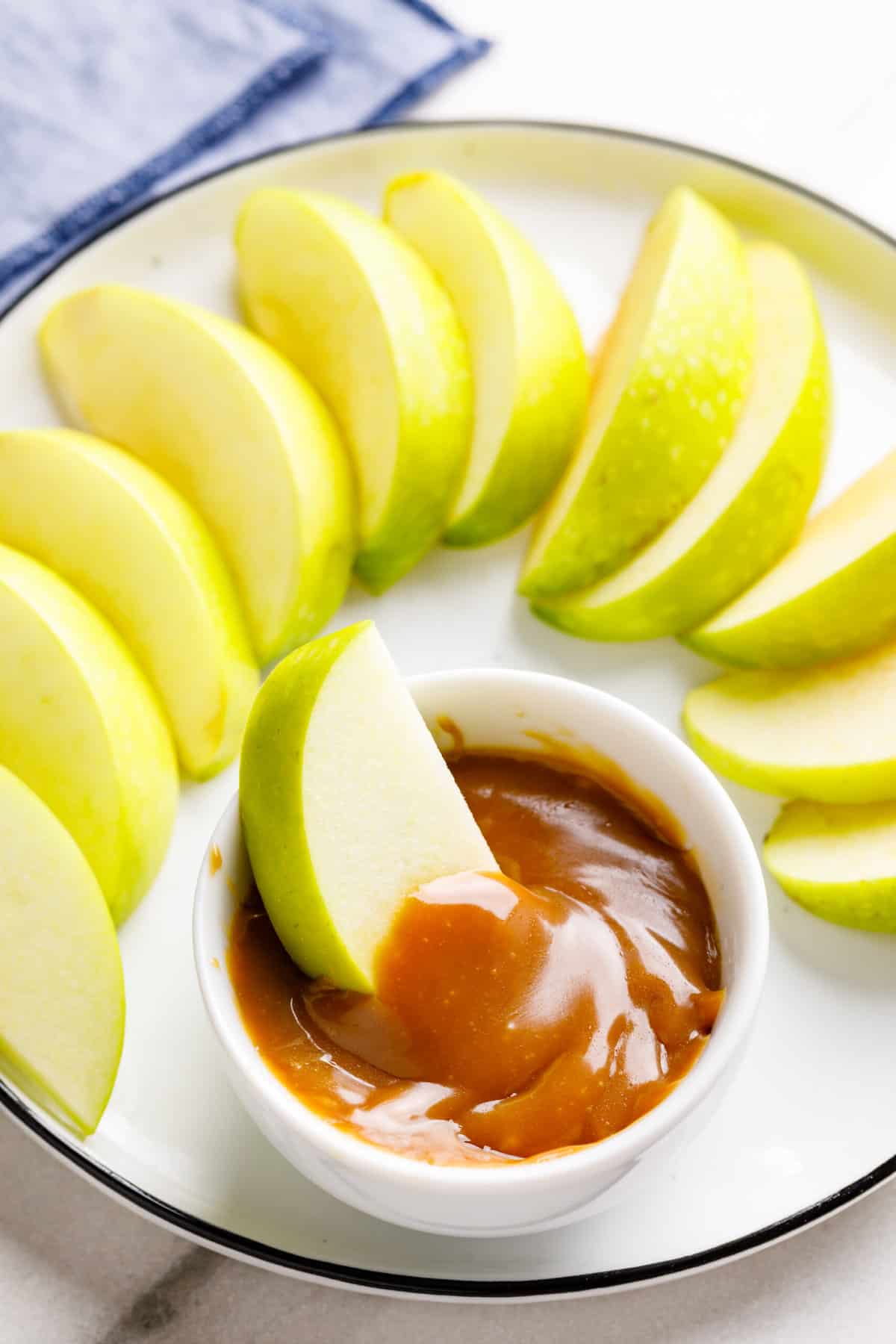 sliced granny smith apples sitting on a white round plate with a side dish of caramel sauce
