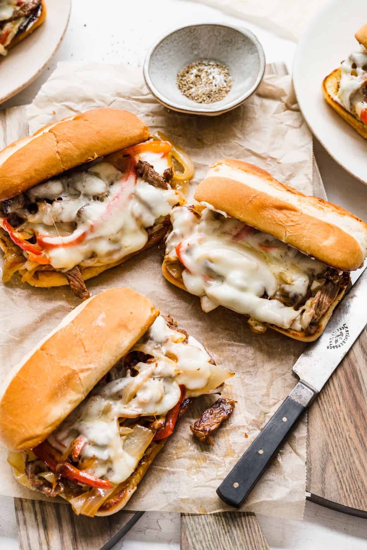 top down image of three philly cheesesteaks sitting on parchment paper on top of a wooden board
