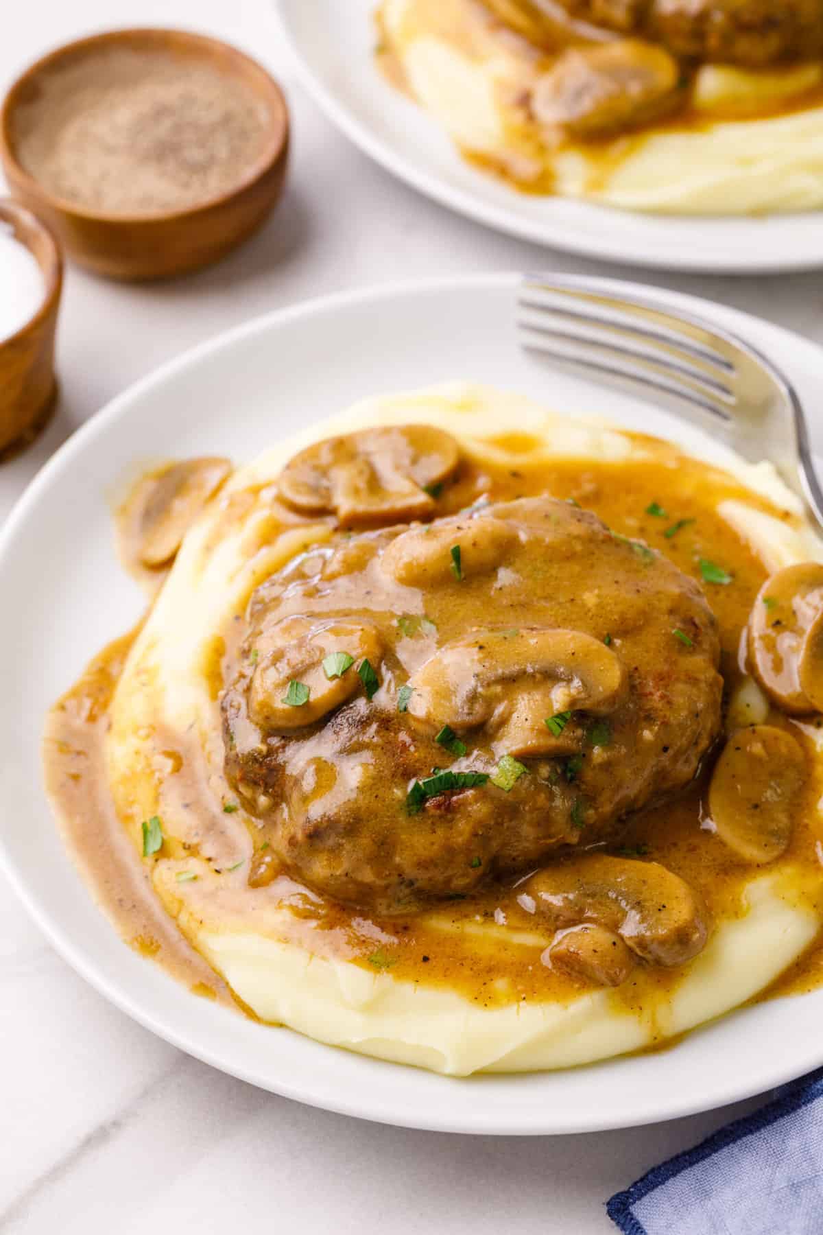 salisbury steak served on a pillow of mashed potatoes sitting on a white plate
