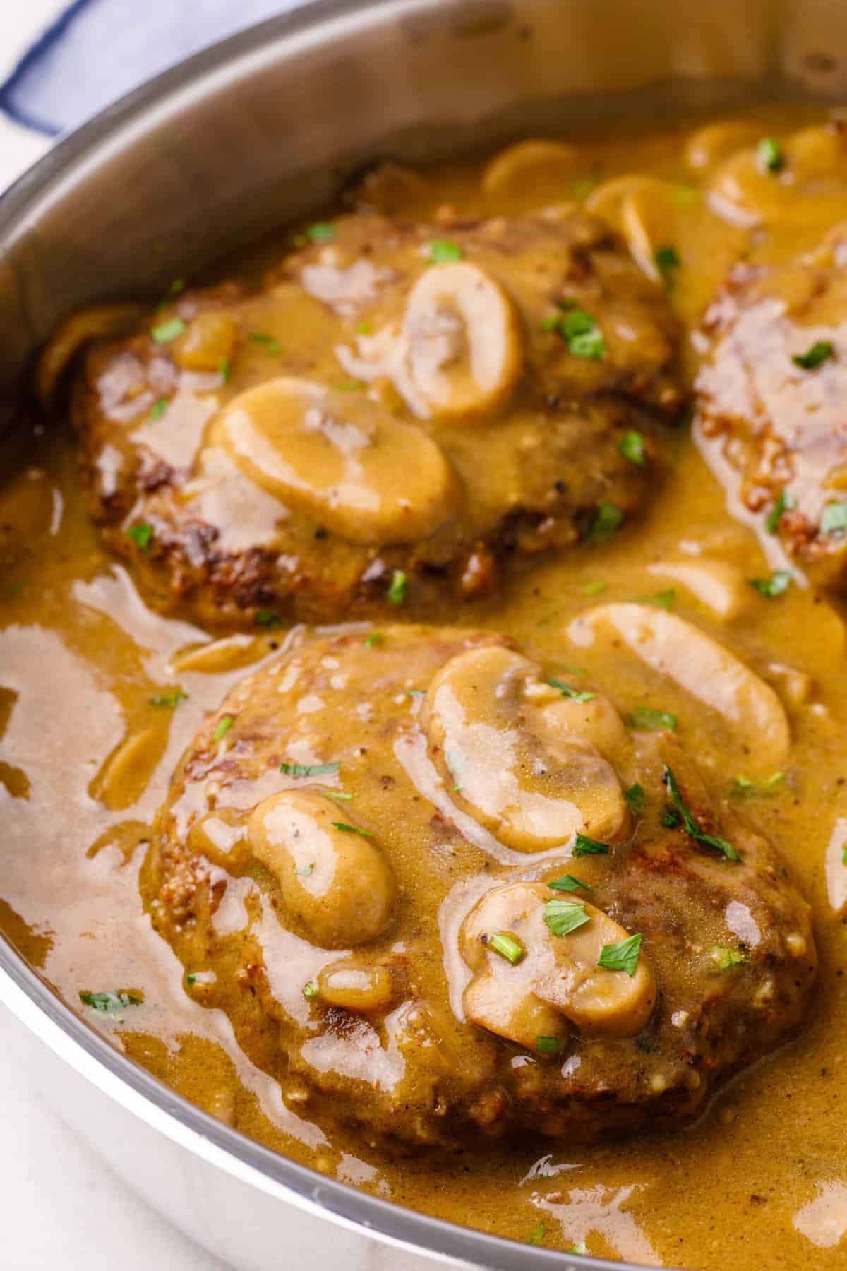 close up of two salisbury steak sitting in mushroom gravy served in a stainless steel pan