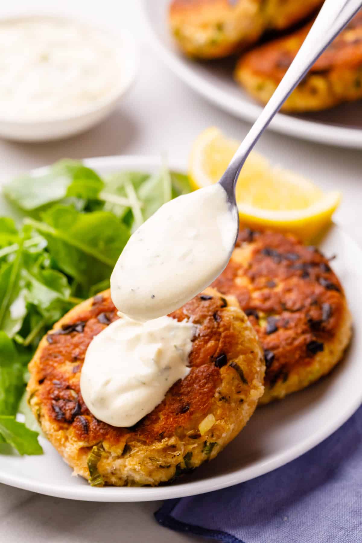 two salmon patties topped with dill sauce and a side of greens served on a white plate