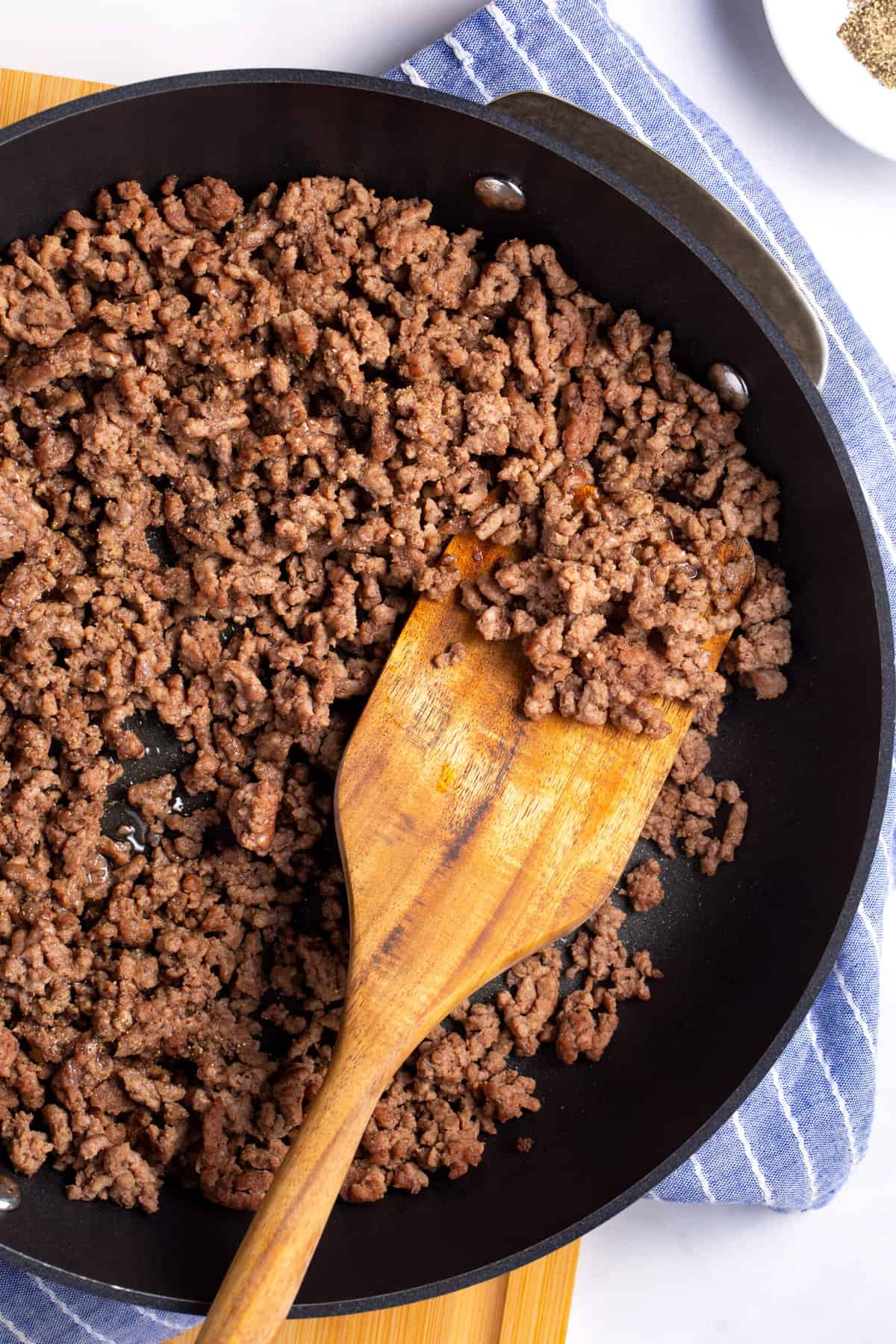 close up top down image of browned ground beef in a pan with a wooden spatula