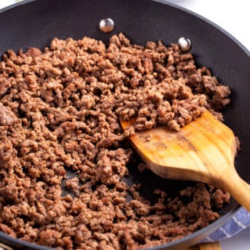 Cooked ground beef in a skillet with a wooden spoon.