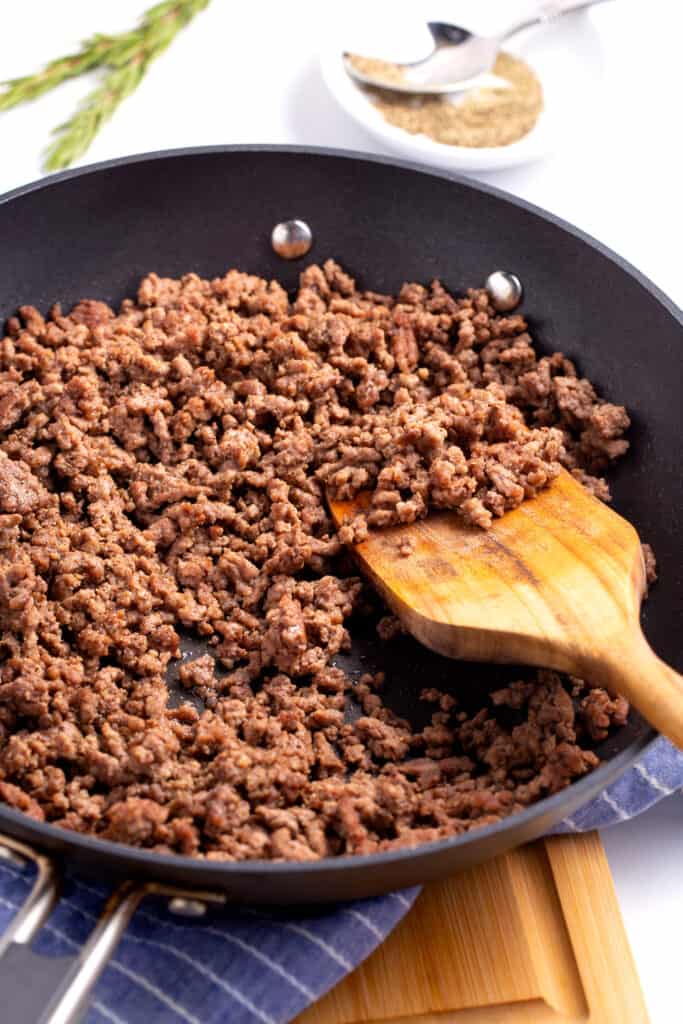 Cooked ground beef in a skillet with a wooden spoon.