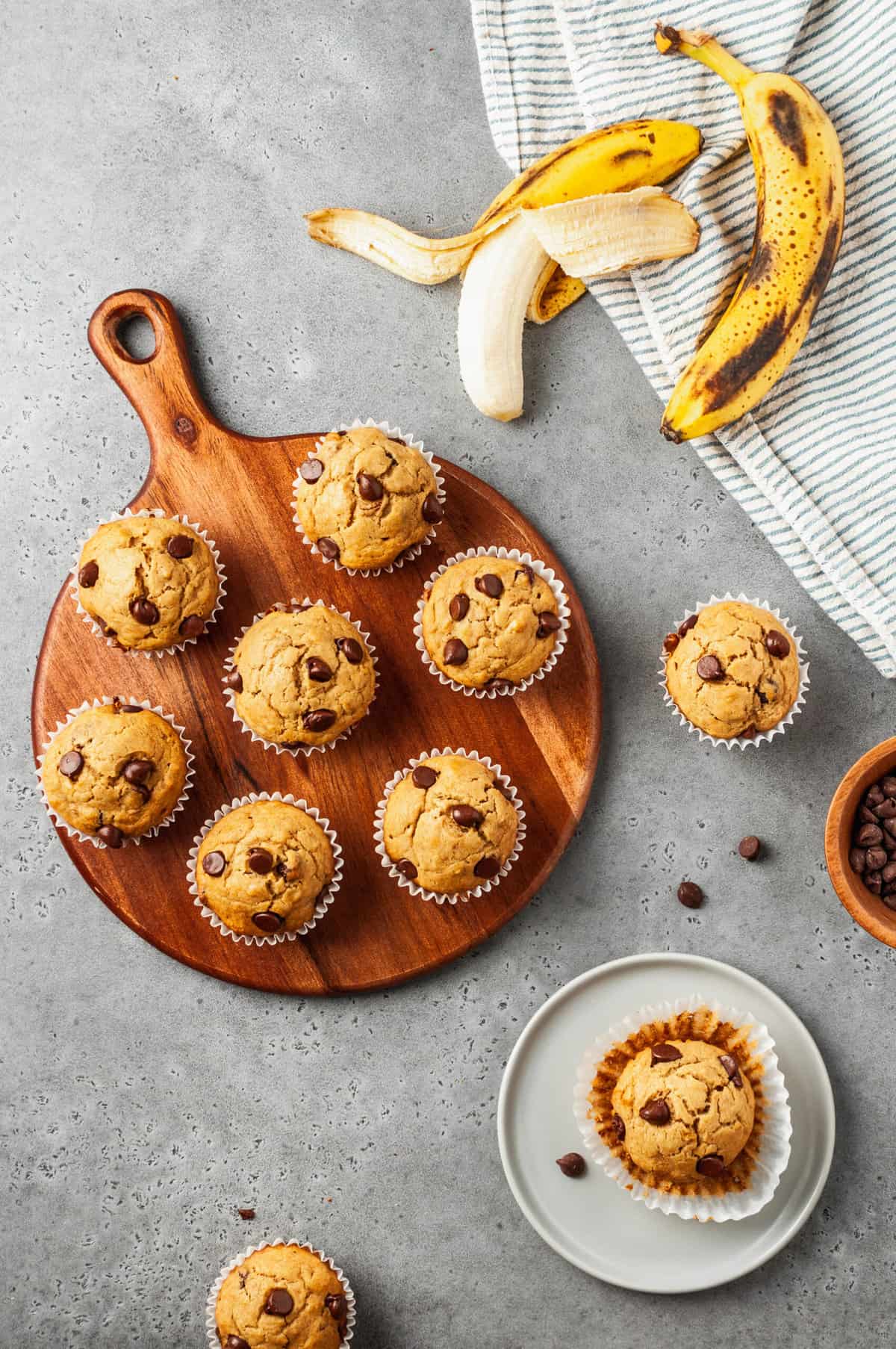 top down image of peanut butter banana muffins sitting on a round wooden platter and one muffin sitting on a grey round plate