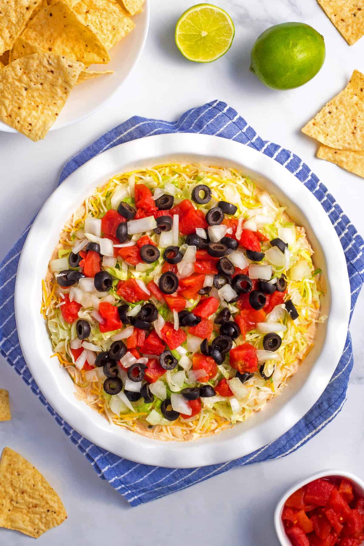 top down image of taco dip in a dish sitting on a blue and white stripe kitchen towel