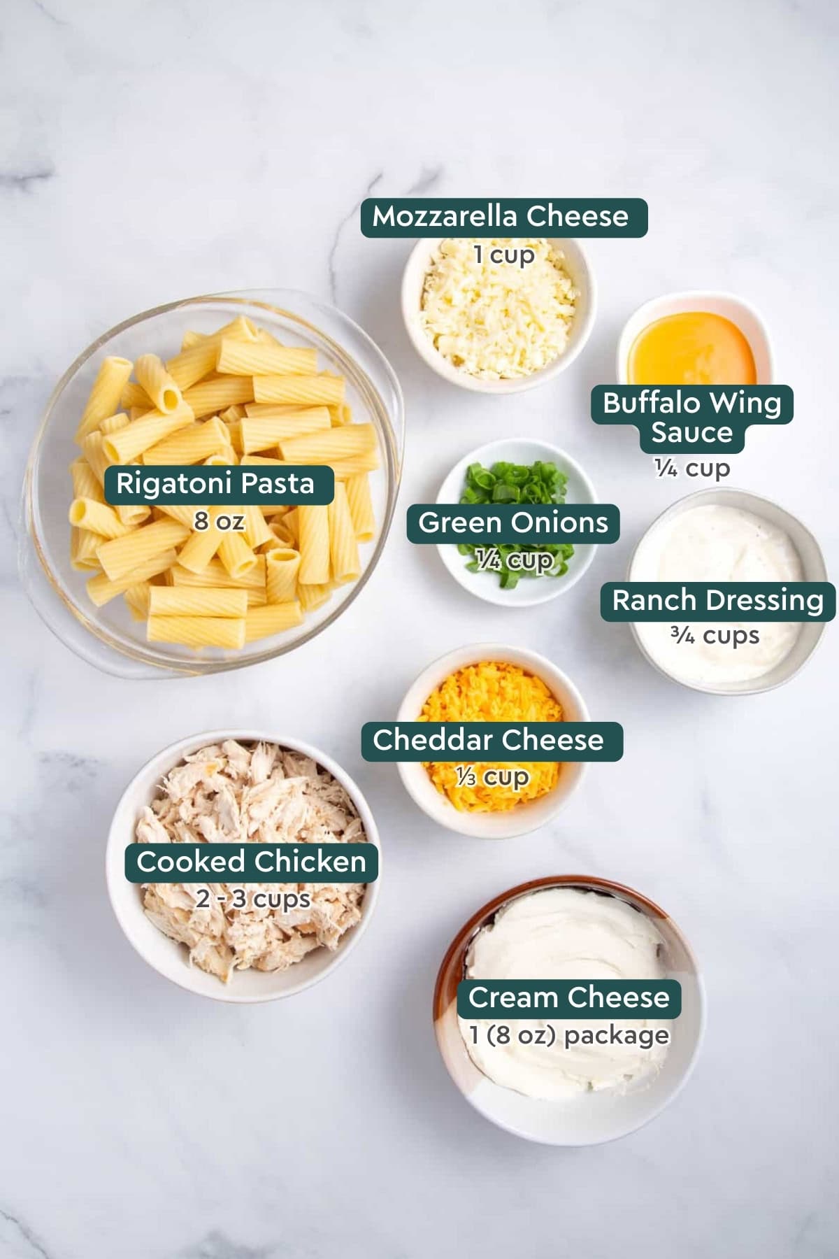 Ingredients for buffalo chicken casserole, including pasta, cheese, wing sauce, green onions, ranch, chicken, and cream cheese.