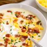 A bowl of creamy cheesy potato soup topped with cheese, sour cream, and bacon.