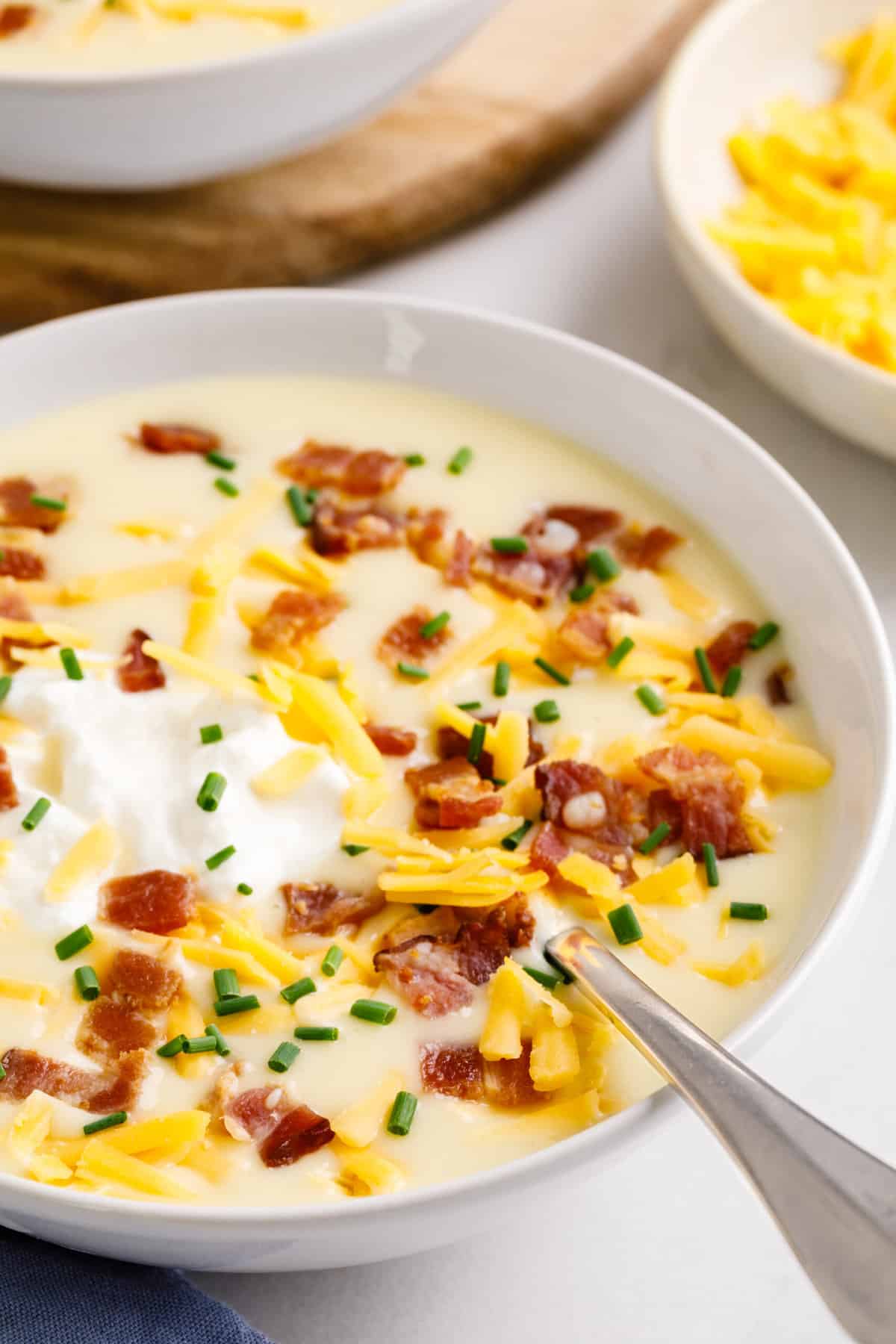 close up image of cheesy potato soup served in a white round bowl