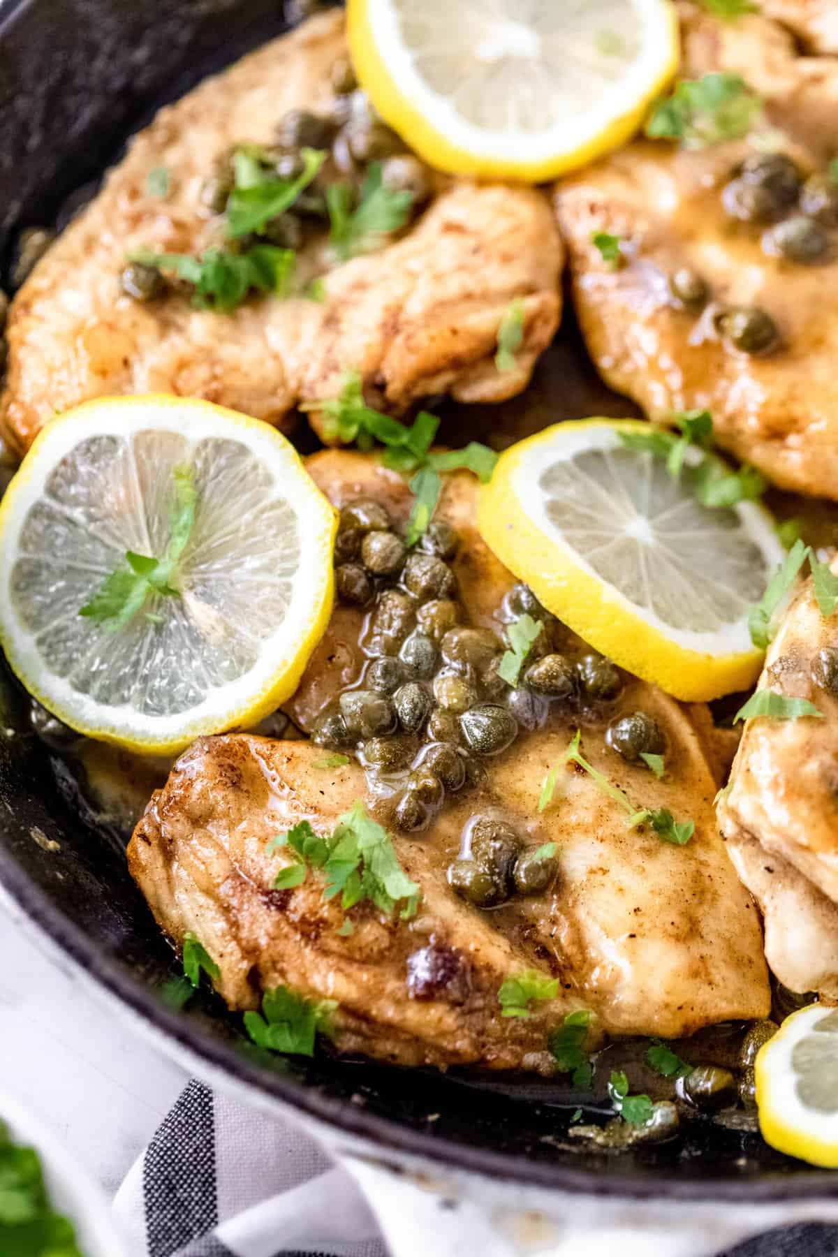 close up of a cast iron skillet with chicken piccata with lemon slices and capers