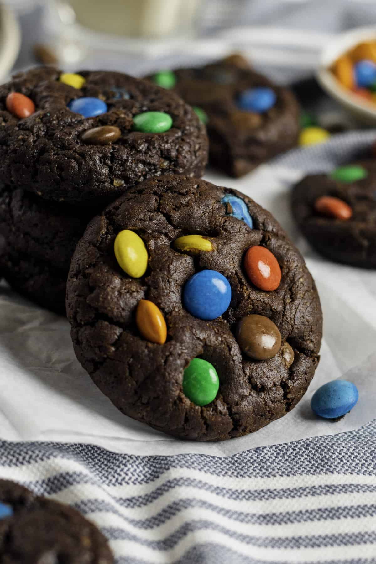 close up image of a chocolate m&m cookies leaning on a stack of other cookies