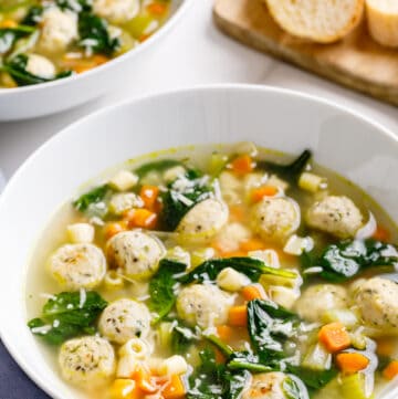 A bowl of Italian wedding soup with a second bowl and bread in the background.