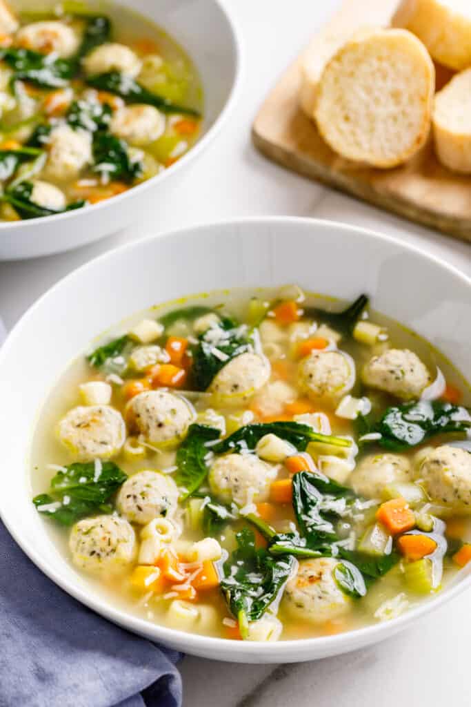 A bowl of Italian wedding soup with a second bowl and bread in the background.
