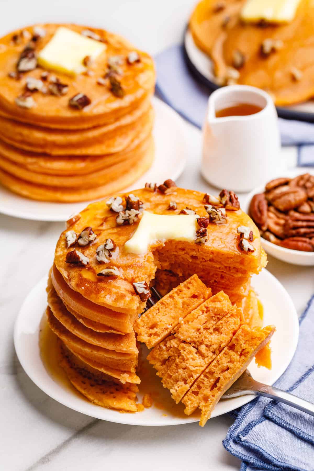 stack of five pumpkin pancakes cut with a knife, showing a forkful of pumpkin pancakes and the cross section of them served on a white round plate