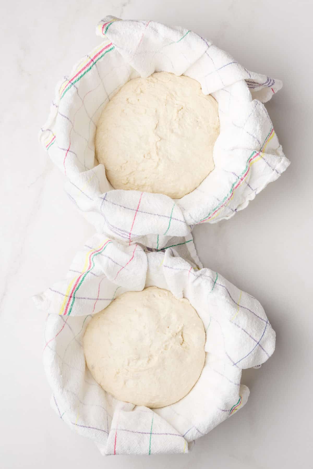 two kitchen towel-lined bowls with sourdough bread dough. 