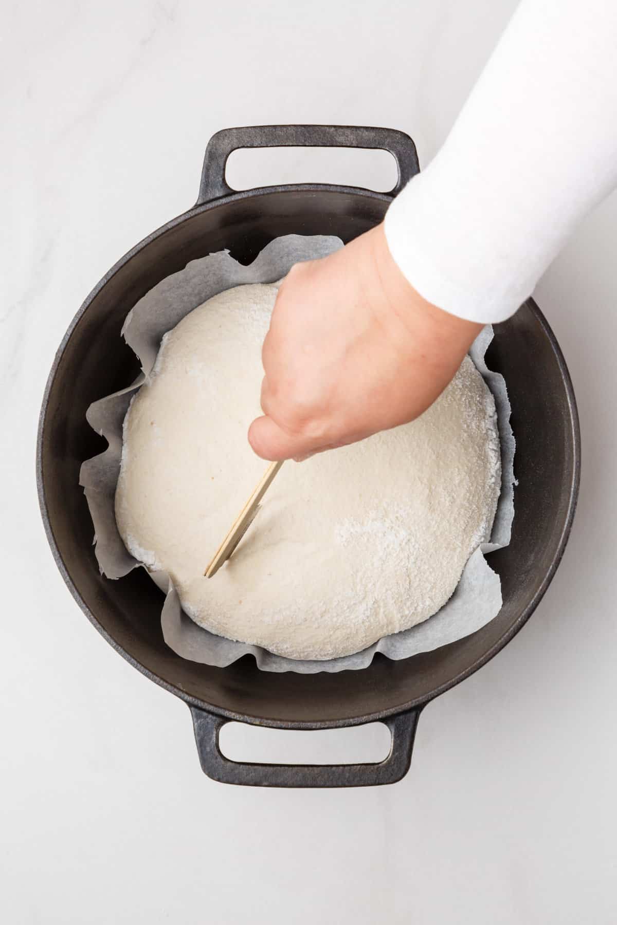 sourdough bread getting scored sitting in a parchment lined dutch oven. 