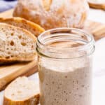 A glass jar of sourdough starter next to a loaf of sourdough bread.