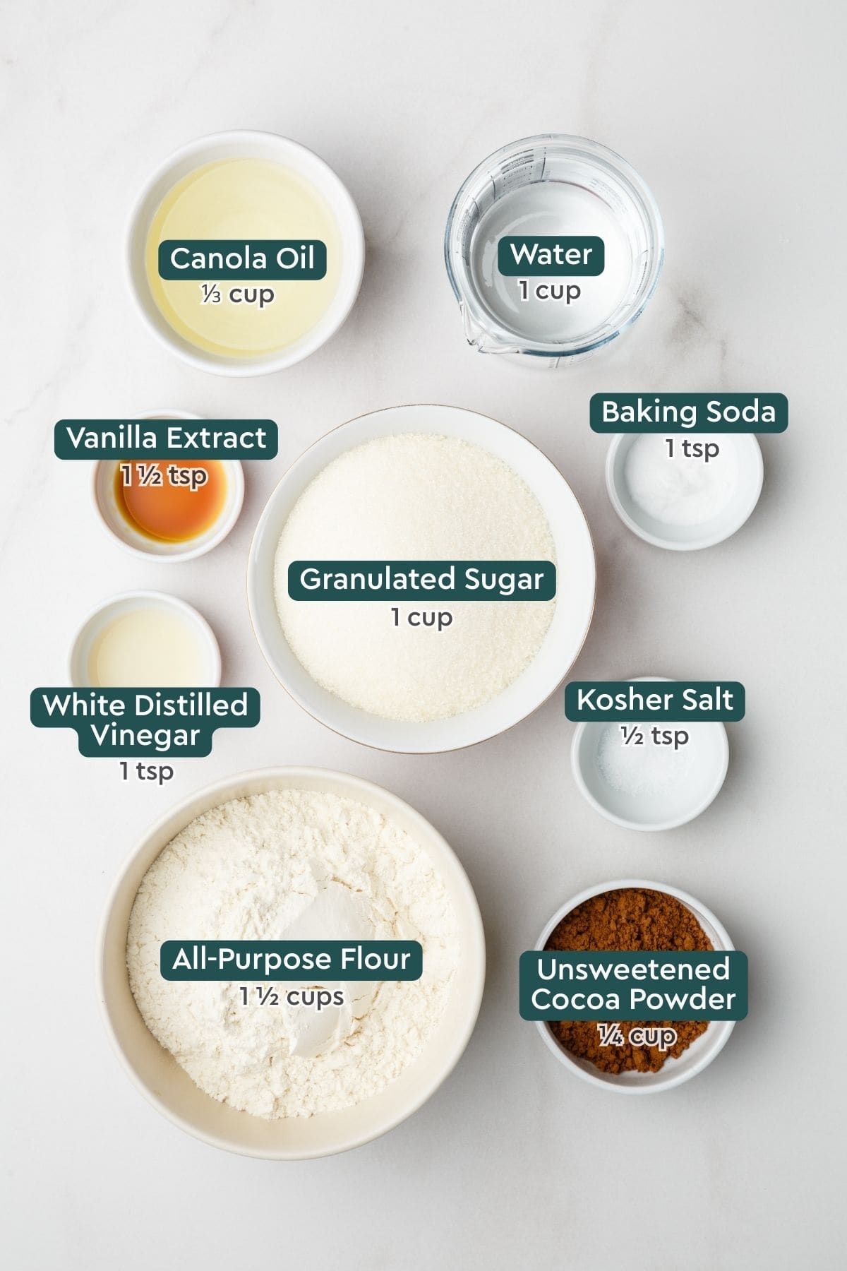 Ingredients for chocolate wacky cake recipe: oil, water, baking soda, vanilla, sugar, vinegar, salt, cocoa powder, flour.