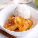Apple dumplings in a white bowl topped with vanilla ice cream.