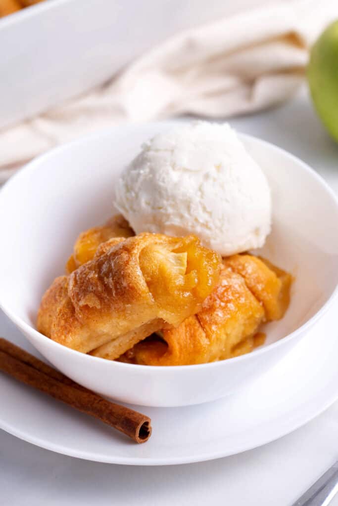 Apple dumplings in a white bowl topped with vanilla ice cream.