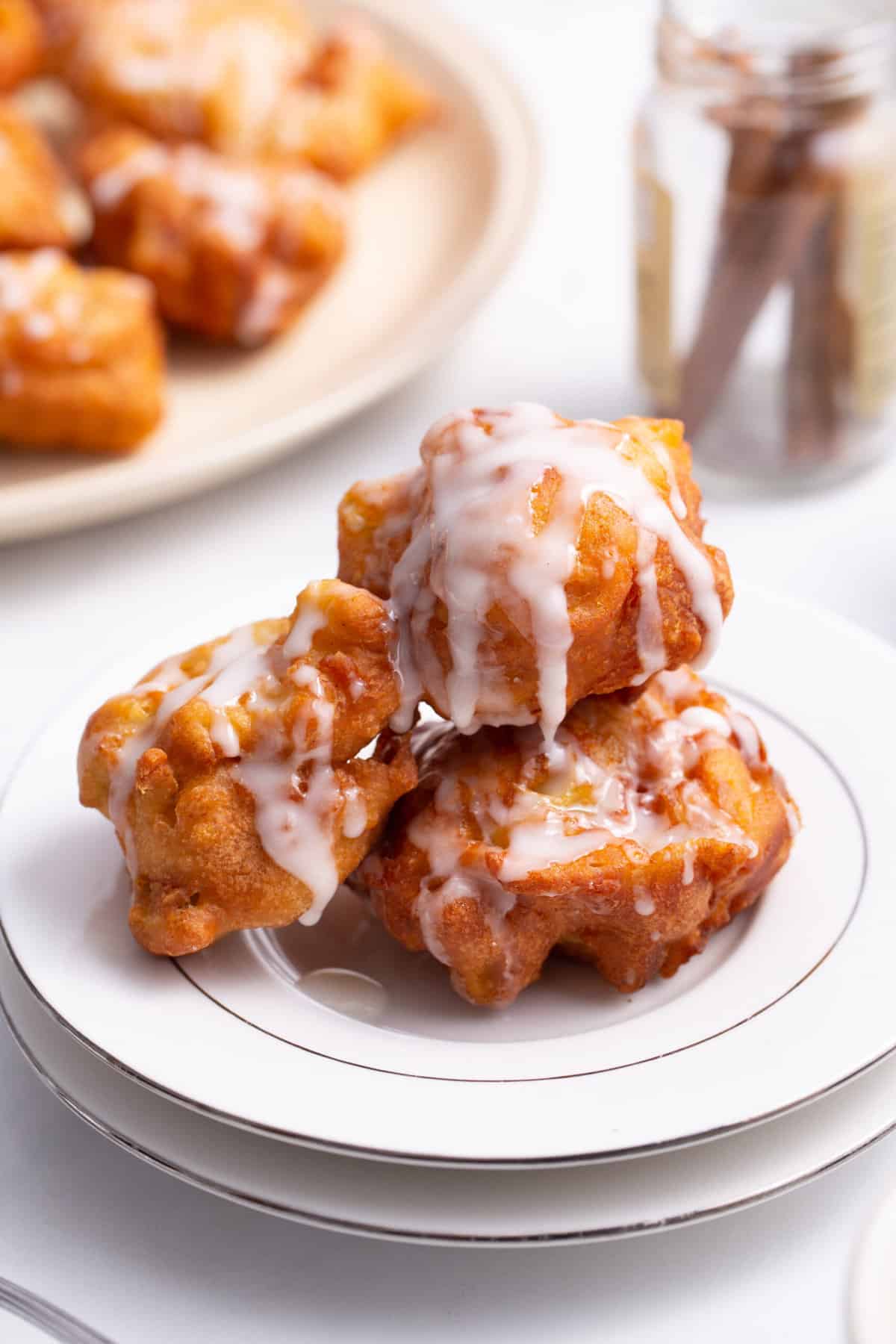 stack of three glazed apple fritters served on a white round plate
