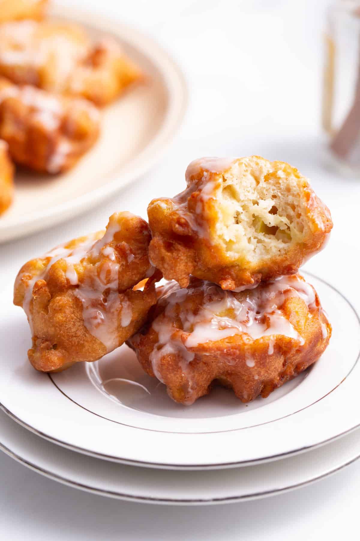 stack of three apple fritters with one having a bite taken out of it all served on a white round plate