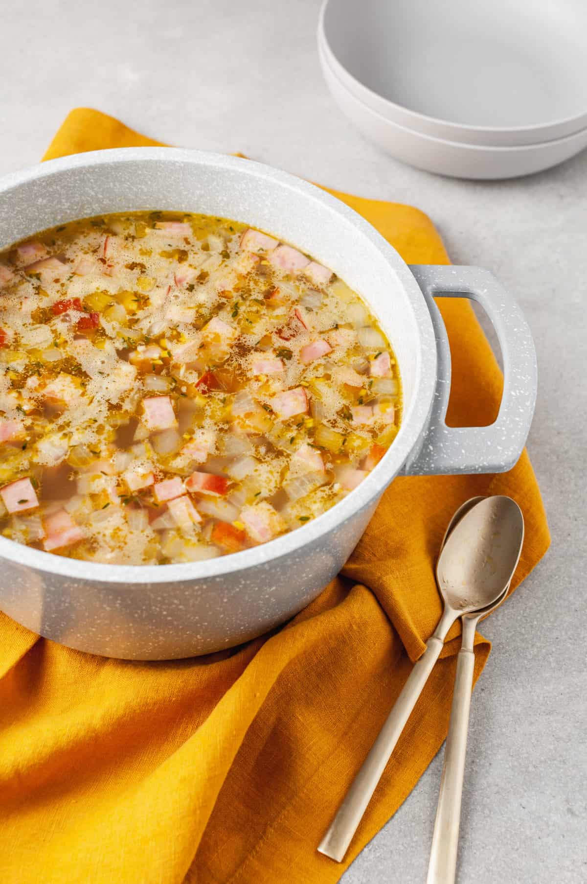 dutch oven full of ham and bean soup sitting on top of an orange kitchen towel.