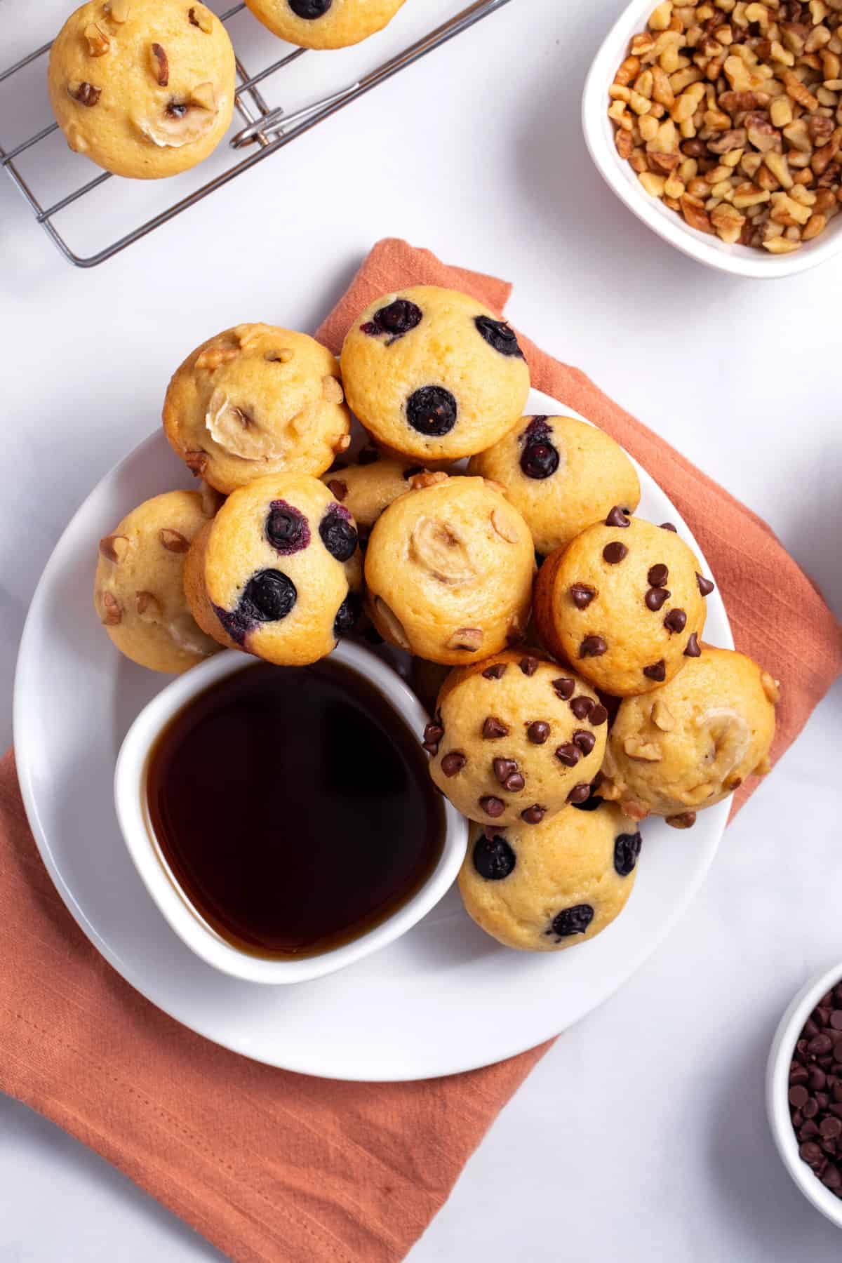 top down image of a variety of pancake muffins served on a white round plate with a side bowl of syrup