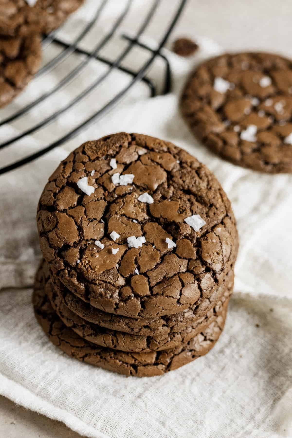 stack of four brownie crinkle cookies topped with sea salt sitting on a kitchen towel