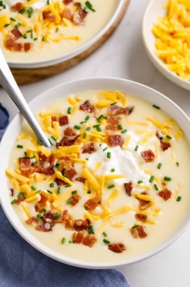A bowl of cheesy potato soup topped with bacon, cheese, sour cream, and chives.