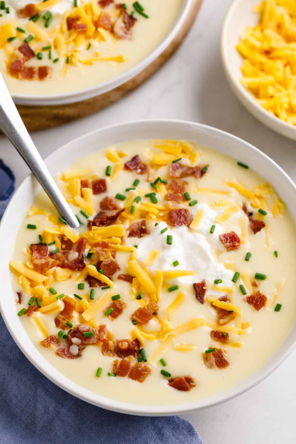 close up image of cheesy potato soup with bacon, sour cream, cheddar cheese, and chives served in a white round bowl