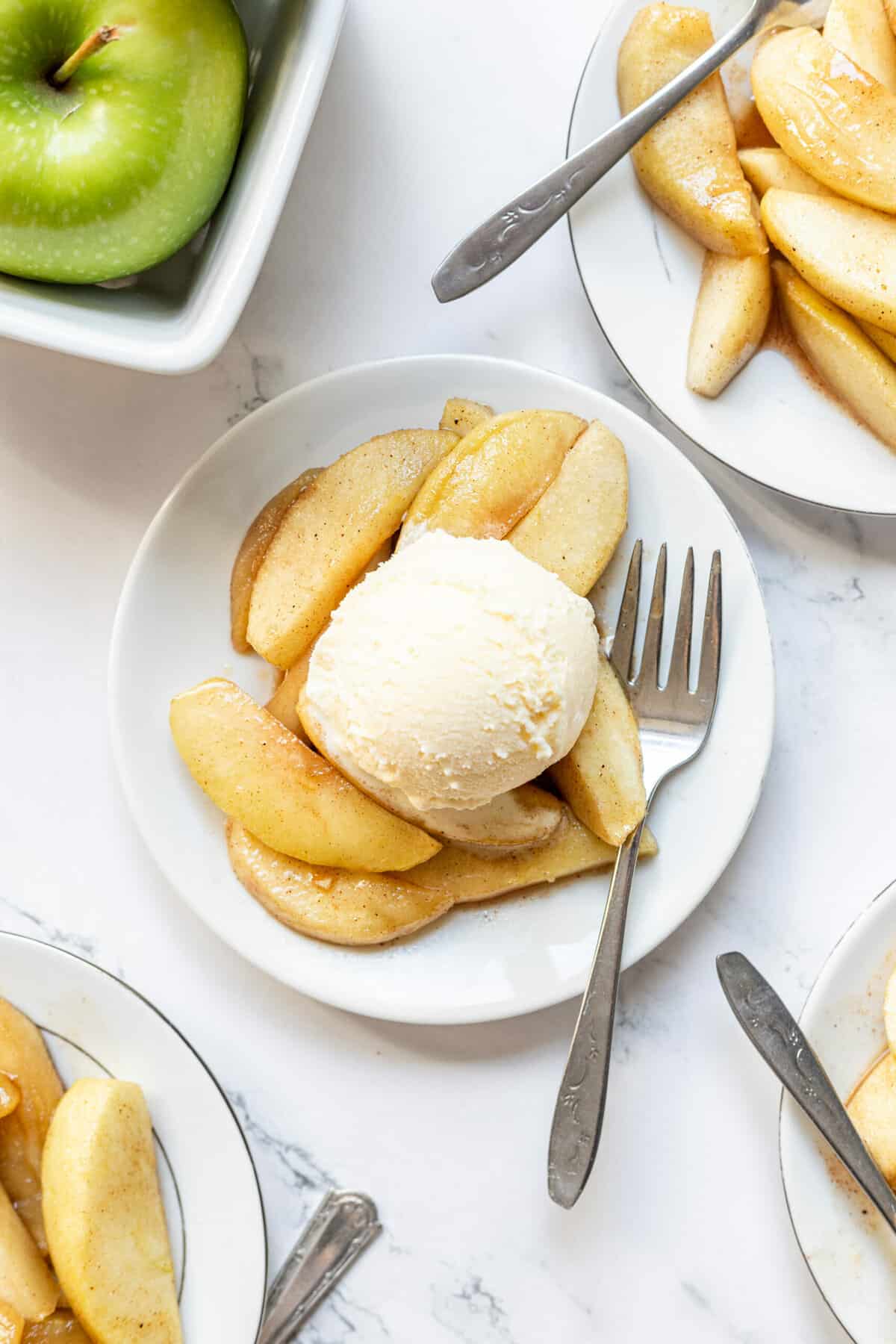 top down image of fried apples topped with a scoop of french vanilla ice cream served on a white round plate with a silver fork