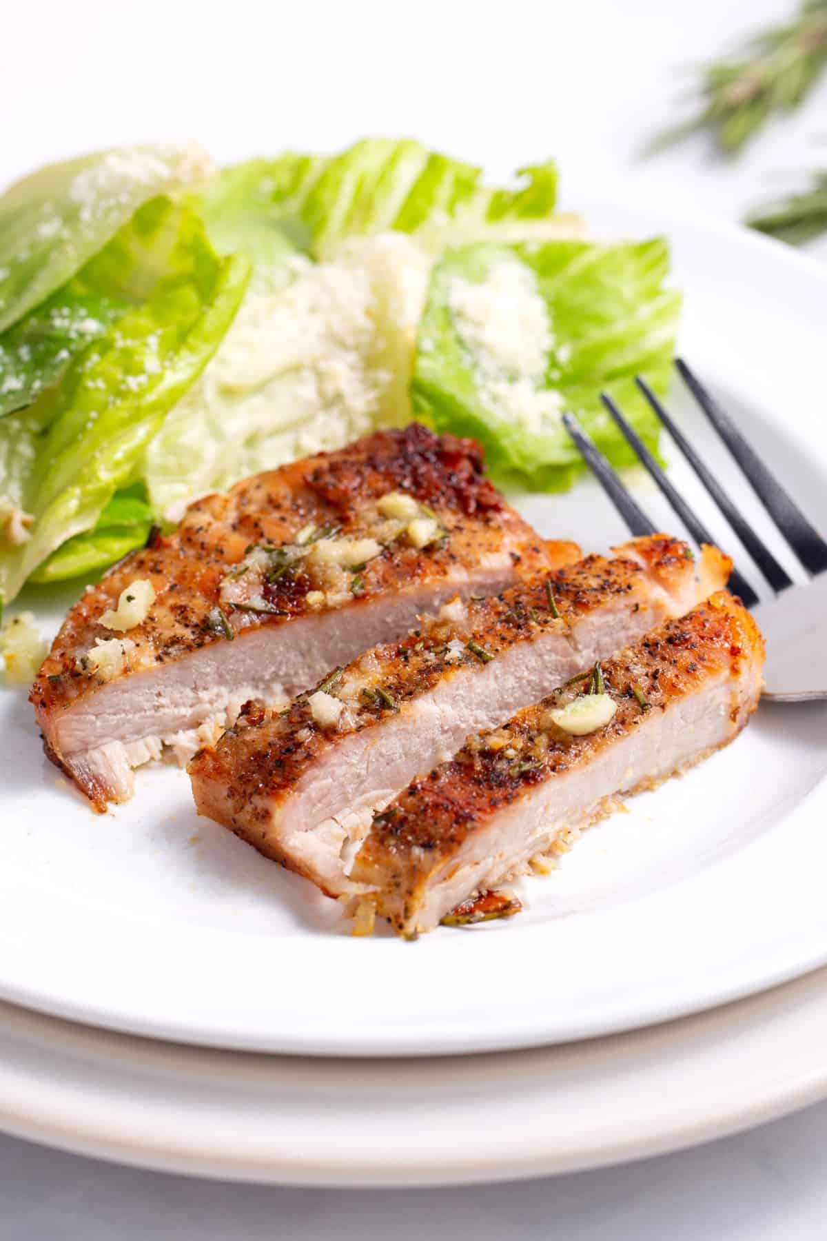 baked pork chop sliced and served on a white round plate with a side salad