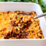 A spoon lifting a scoop of cheeseburger casserole from a baking dish.