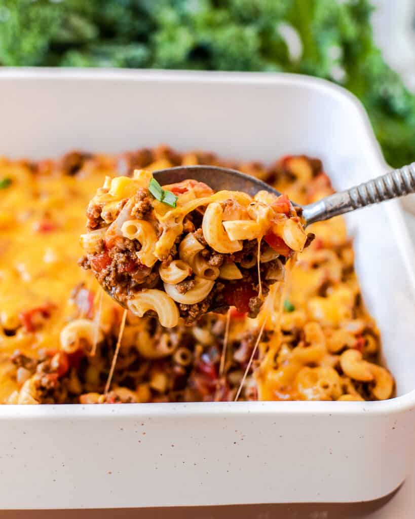 A spoon lifting a scoop of cheeseburger casserole from a baking dish.