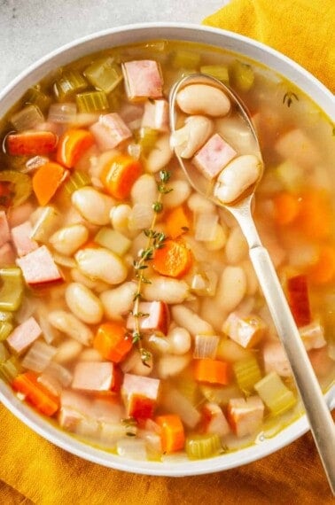 A bowl of ham & bean soup with a spoon lifting a bite.